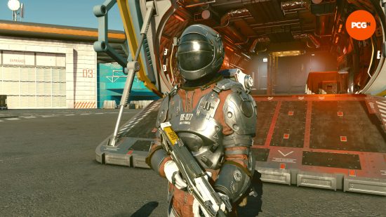 A person covered head to toe in a space suit made from the toughest materials, making it great for the best Starfield tank build. They're beside their spaceship hangar.