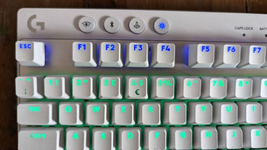 Logitech G Pro X TKL Lightspeed review: the top left of a white keyboard with blue and turquoise RGB lighting is shown above a wooden worktop.