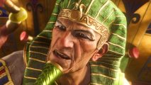 Total War Pharaoh campaign - A Pharaoh wearing a green and gold headdress talks vigorously to a grape pinched between his finger and thumb.
