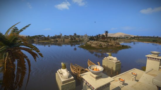 Total War Pharaoh campaign - A town built on the banks of a river. Boats rest at a dock by blazing fire pits.