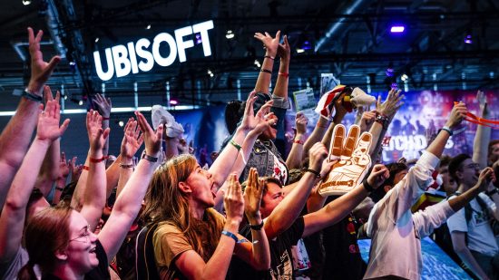 A crowd of people cheers and raise their hands with a huge Ubisoft logo in the background