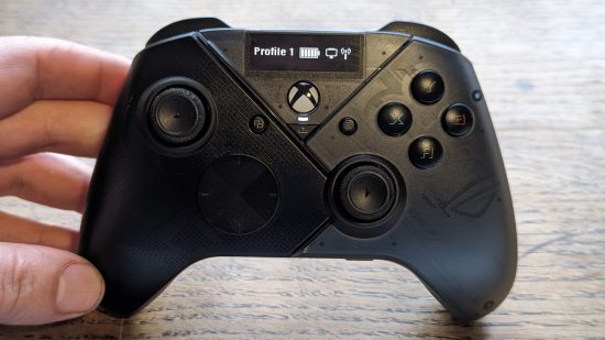 Asus ROG Raikiri Pro review: a black controller appears on a wooden desk with a hand holding it up.