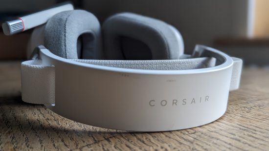 Corsair HS80 Max review: a white headset with retracted microphone appears from above on a wooden table.