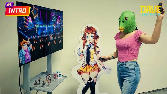 Actualización de octubre de Dave the Diver: una persona que lleva una máscara de pez de goma muestra la versión del juego para Nintendo Switch, de pie junto a un recorte de una de las chicas de StraStella, el anime favorito de Duff.