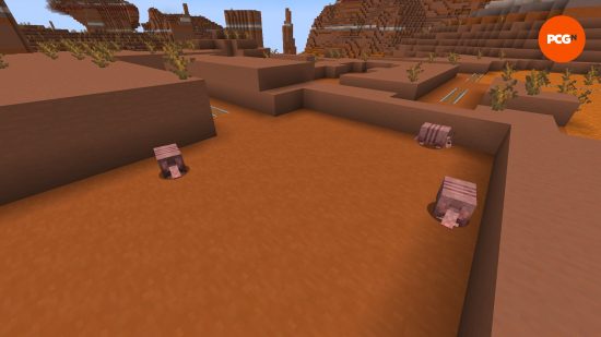 Three Minecraft armadillo appear above a cave entrance in a badlands biome.