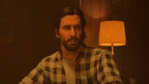 Alan Wake 2 Sam Lake wikis: a man with shoulder length black hair and a short beard sat at a table wearing a black and white chequered shirt