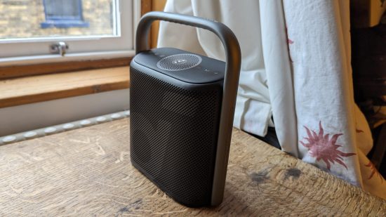 Anker Soundcore Motion X500 review: a black speaker with silver handle appears from the side against a wooden surface.
