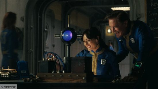 A man and a woman, dressed in blue and yellow. The man is standing, the woman is setting at a desk. There are vault control panels around them. 