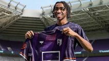 A young Black male smiling as he proudly holds up a football shirt for his new club