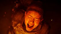 Hellblade 2 launch date: A woman engulfed by fire screams, her eyes shut tightly as embers fly up around her