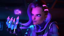 Overwatch 2 quicker play: A woman with swept-back short purple hair and a mech-like hand wields a glowing violet cube, her eyes fixated on it as it floats above her right palm