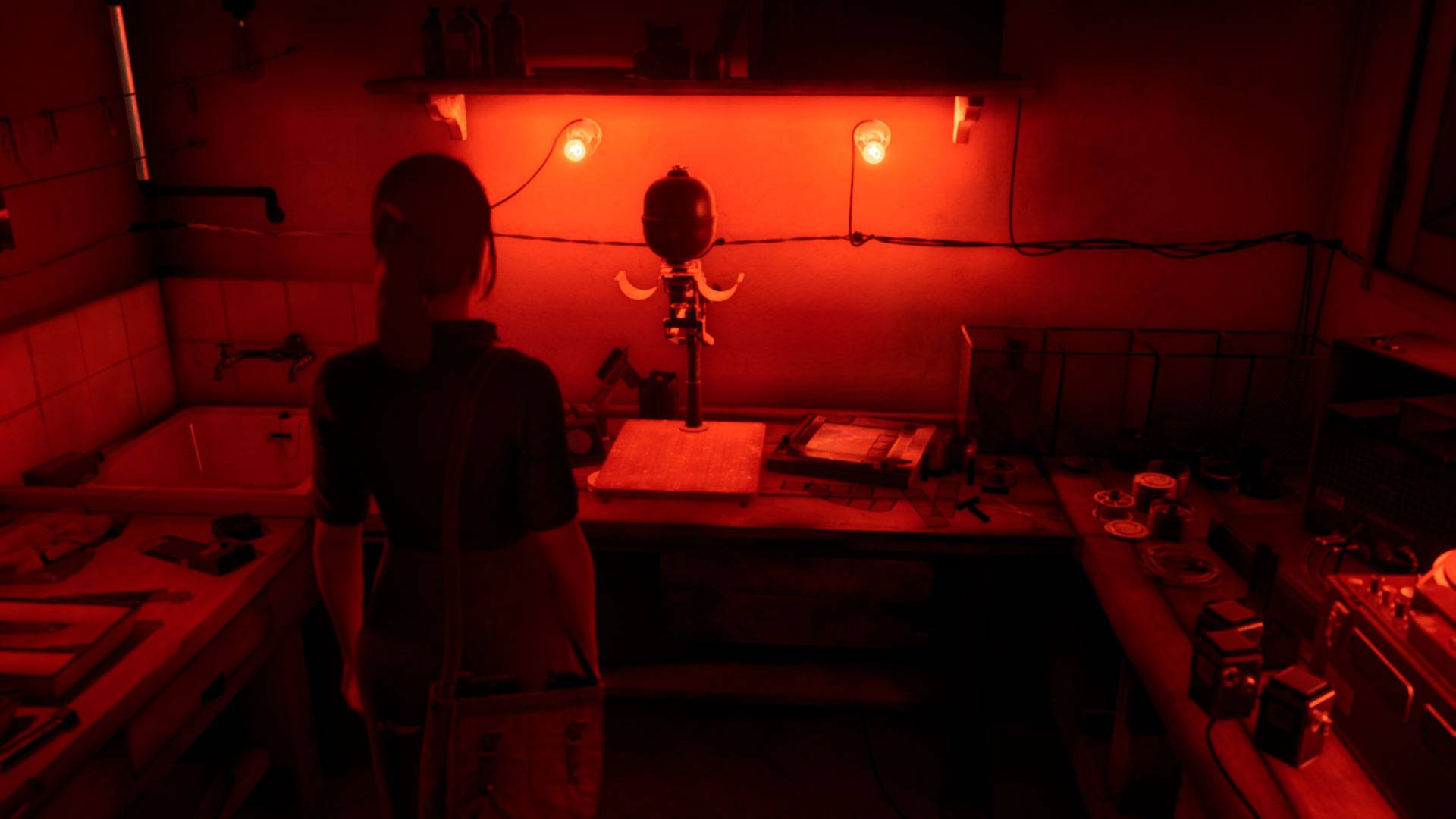 Una mujer joven con el pelo recogido se encuentra en una sala de fotografía con un equipo antiguo frente a ella, iluminado en rojo.