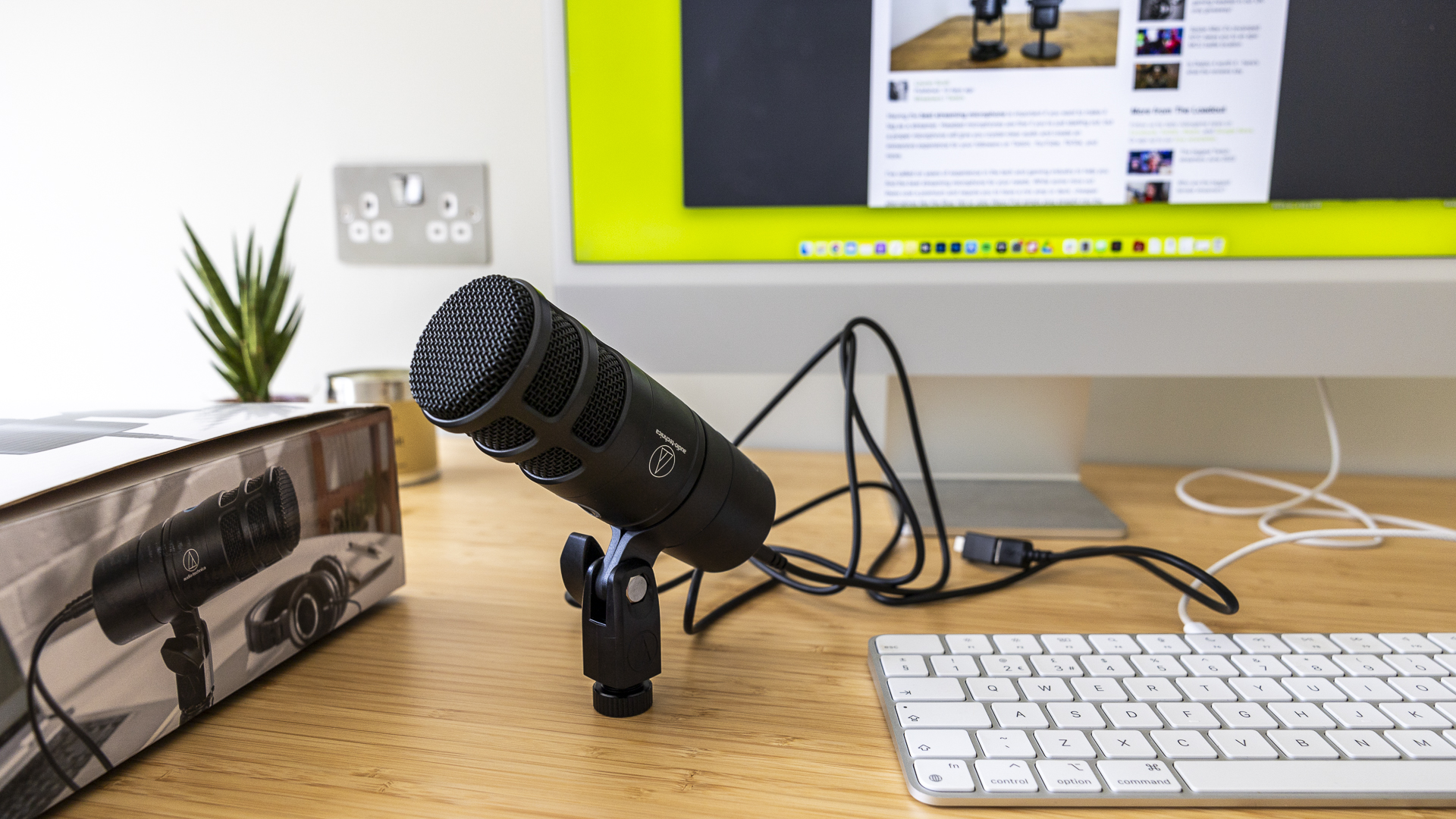 Audio Technica review image showing the microphone on someone's desk near a box and a keyboard.