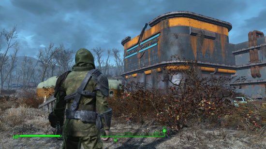The player stands wearing green fatigues and a hood, facing a blue and orange building. ‘ArcJet Systems’ is written on the sign at the top of the building.