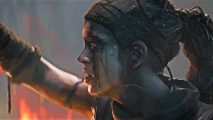 Senua stares up at an unseen foe as a fire rages around her in Hellblade 2.