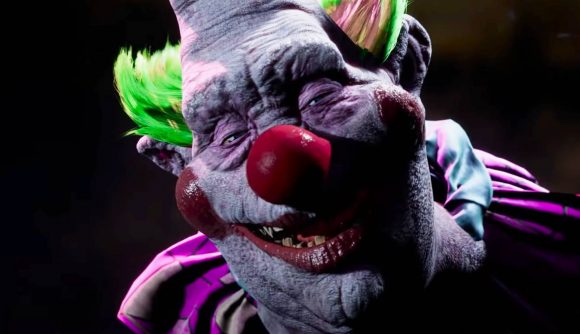 A creepy clown with green tufted hair and a huge red nose grins menacingly into the camera