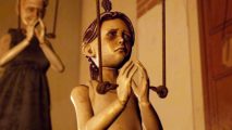 A wooden puppet puts its hands together in prayer, a sad expression on its face