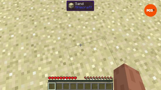The player looks at the ground, and a UI at the top of the screen shows they are looking at a block of sand thanks to Waila, one of the best Minecraft mods.