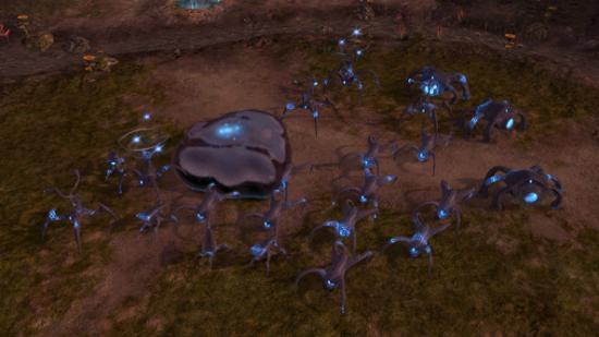 On a brown rocky plateau, a bunch of spindly blue-gray machines with not visible moving parts stand next to a metallic blob of the same color.