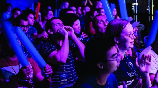 A crowd of nerds illuminated by purple LEDs watch the WCS America Finals, cheering and screaming.