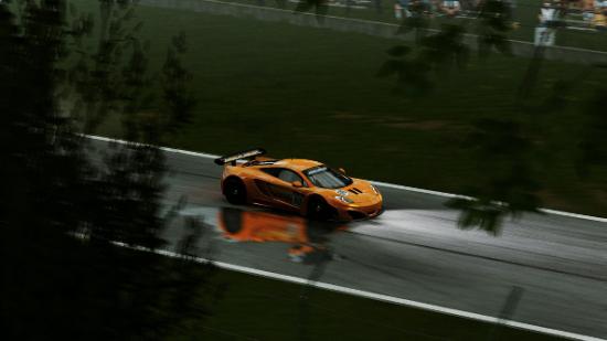 An orange sports car races through a rainy German forest racetrack.