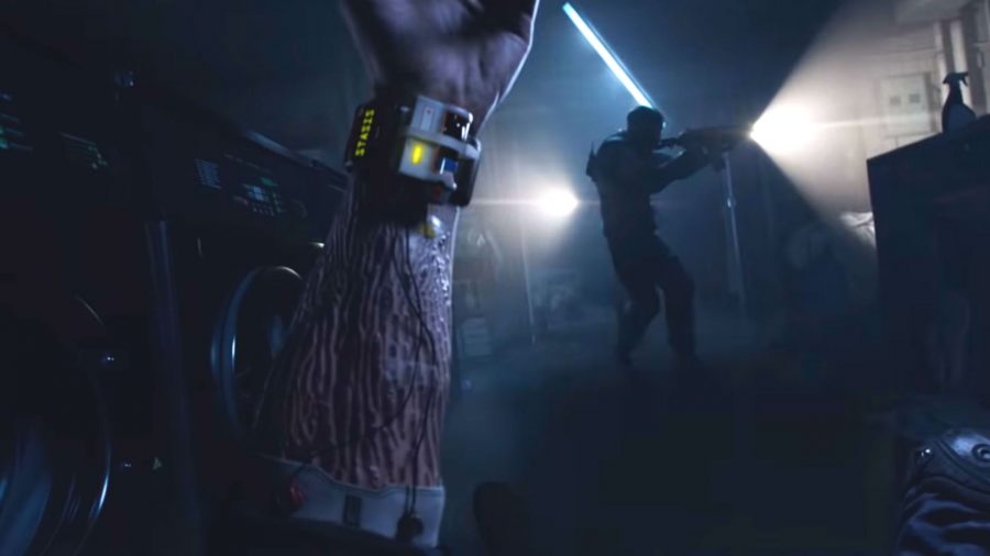 Foreground: A marked arm wearing a strange watch-like contraption. Background: an operative with a gun