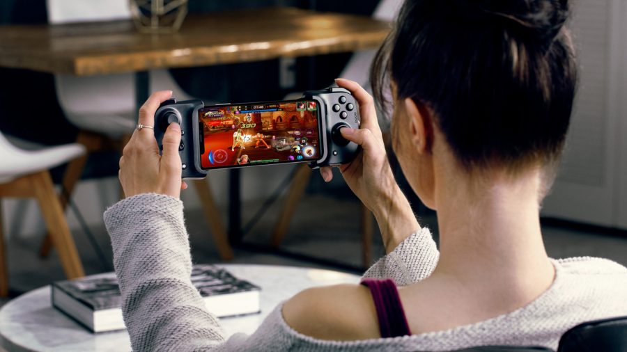 A woman plays a PC game on her smartphone using the Razer Kishi controller