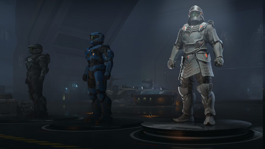 Three armour cores lined up in the middle of a dark facilities with vehicles in the background