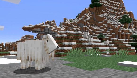 Mountain goats graze on a snowy mountainside in Minecraft.