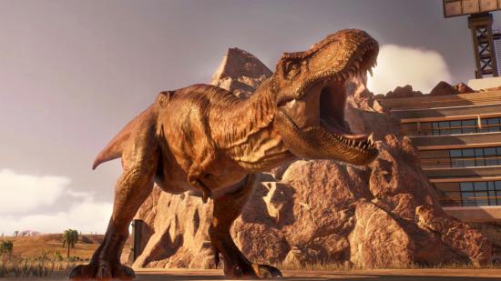 A Tyrannosaurus Rex roars in the Jurassic Park San Diego scenario within Jurassic World Evolution 2's Chaos Theory scenario mode. The scene is bathed in the orange glow of a setting sun, and behind the roaring dinosaur is a rock which shelters the park's amphitheatre