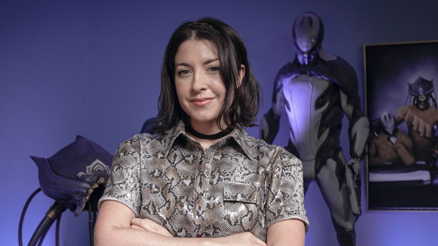 Warframe's Rebecca Ford, standing by a Warframe in the Digital Extremes studio