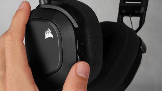 A person holds the left ear cup of the Corsair HS80 gaming headset