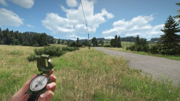 A hand holding a military-style compass near a gravel road in a sunny field in Arma Reforger
