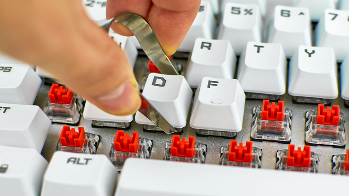 How to clean keyboard: hand with keycap puller on white keyboard with red switches