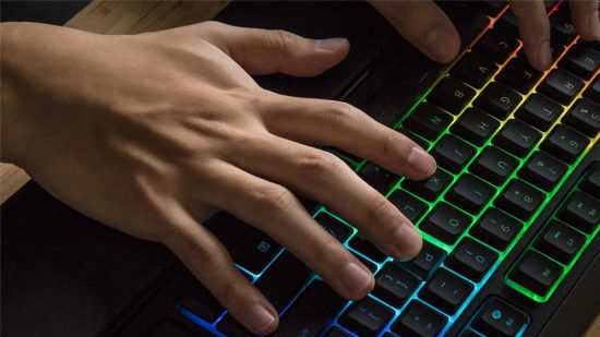 A League of Legends player positions their fingers over the keyboard lit up with RGB