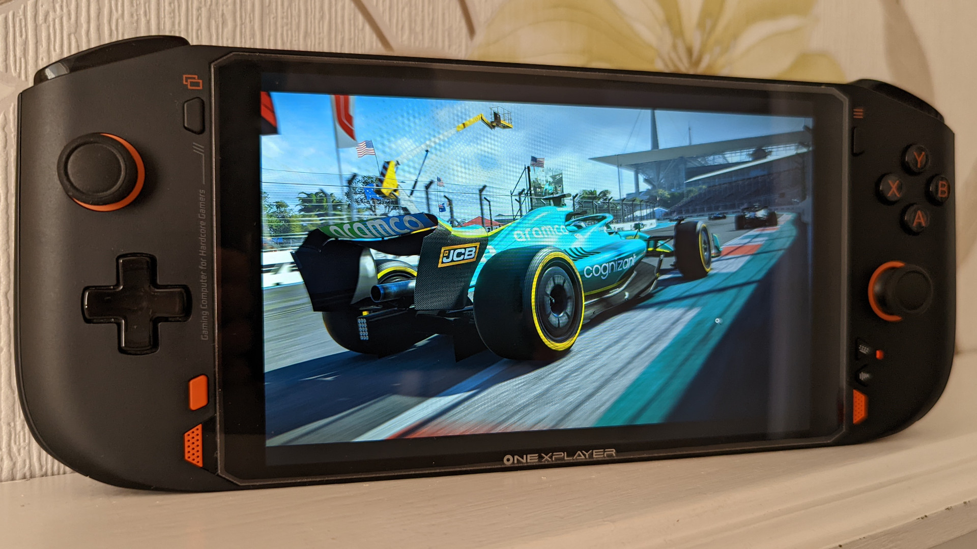 OneXPlayer Mini AMD review: The portable powerhouse sits atop a white surface, with images of a blue F1 car racing down the track showing on its display