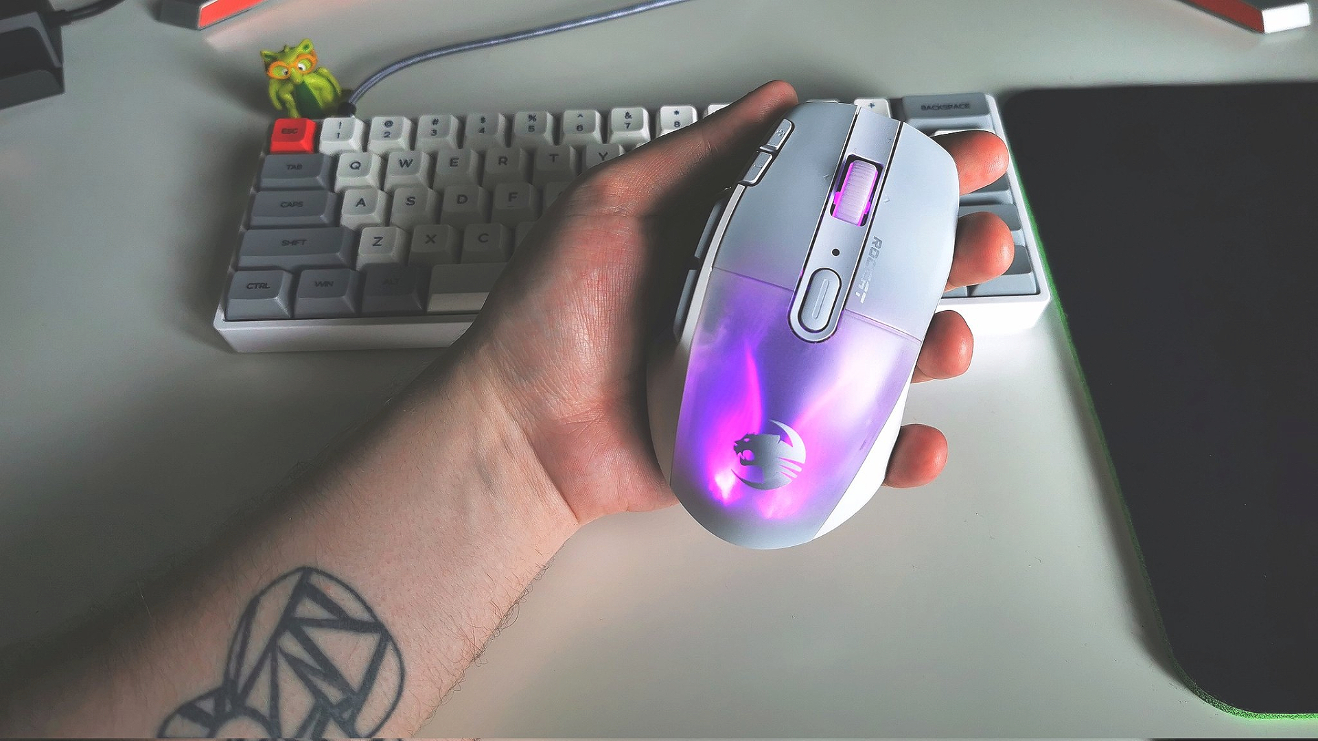 Hand holding Roccat Kone XP Air gaming mouse next to white keyboard